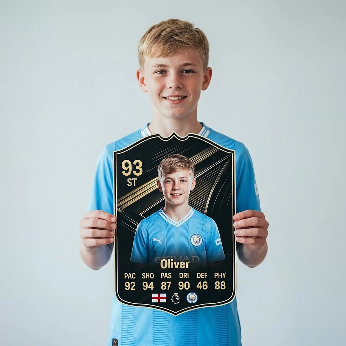 Chico con camiseta del Manchester City sosteniendo su carta de FIFA FC 26 Team of The Week personalizada — CardsGoat