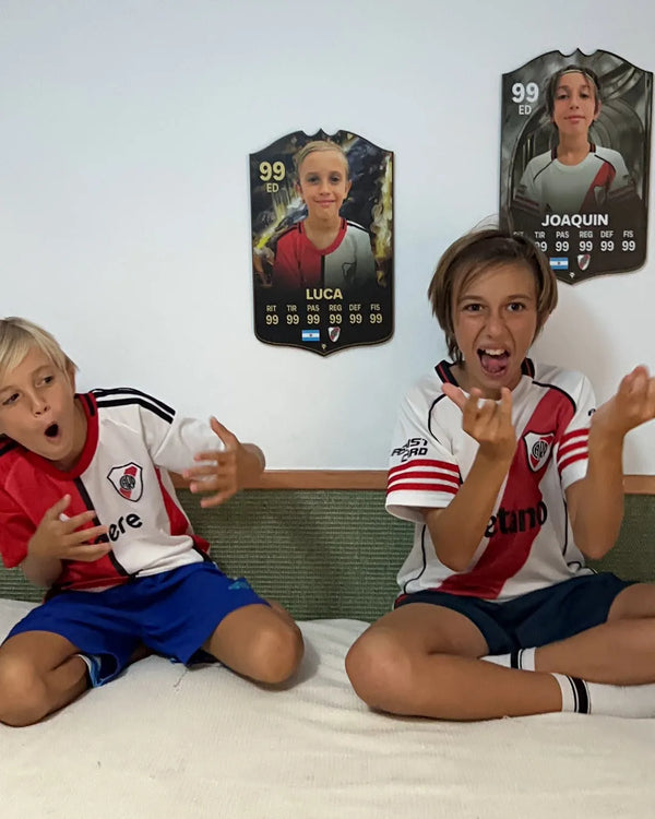 Dos niños con camisetas de River Plate celebrando delante de sus cartas FIFA personalizadas colgadas en la pared — clientes de CardsGoat